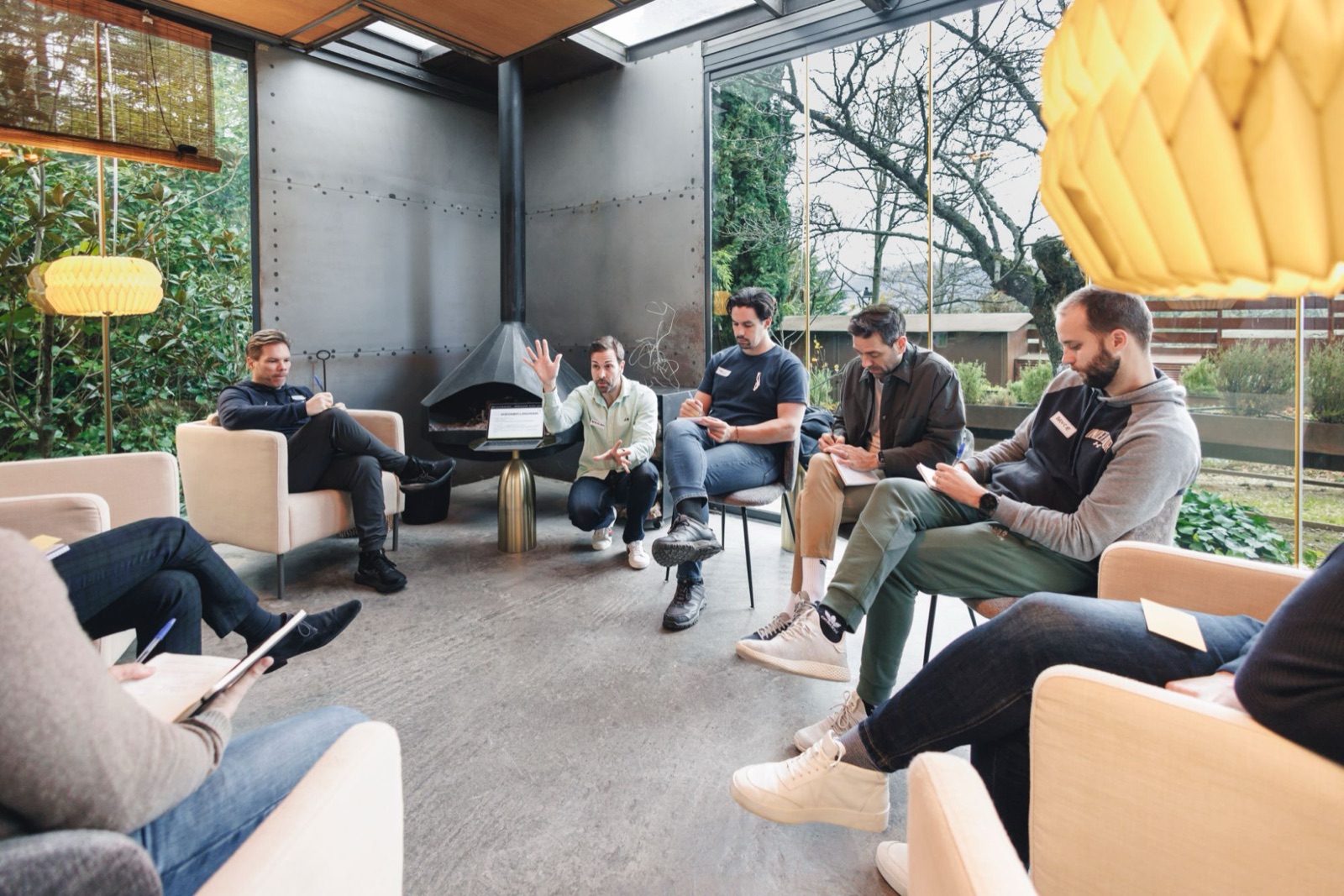 Jose M Bermejo crouches in a circle of leaders taking notes, in a glass room with a fireplace, during a working session.